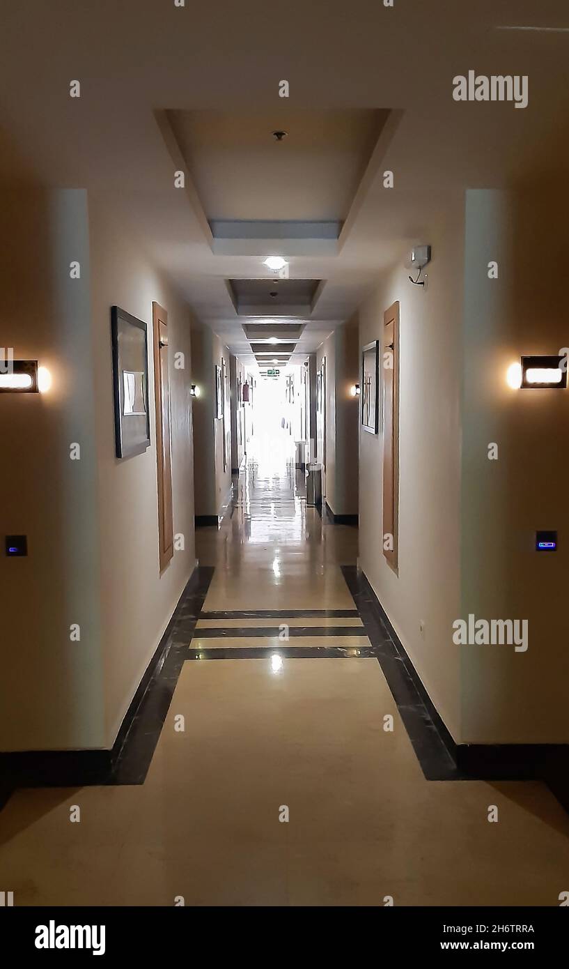 Long couloir menant à la perspective, une rangée de pièces sur les côtés, lumière vive à la fin tout est éclairé par des lampes Banque D'Images