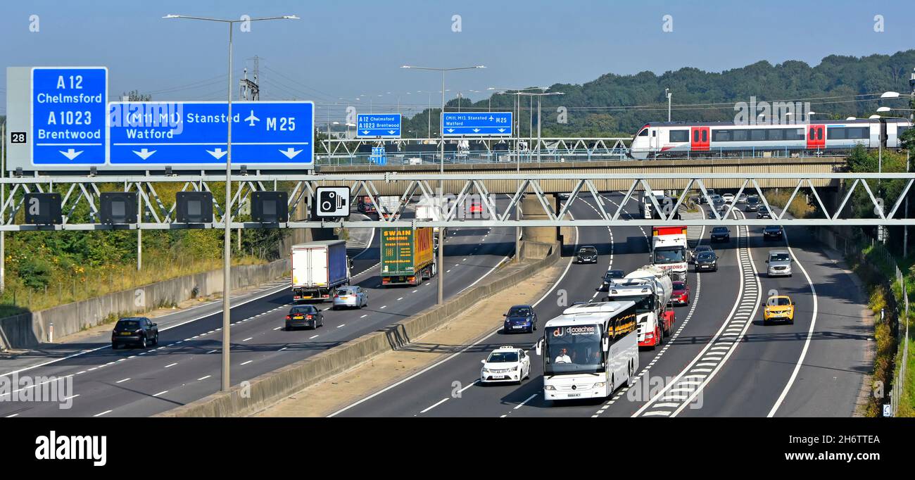 Train de voyageurs Greater Anglia traversant le pont ferroviaire au-dessus de la jonction de la circulation routière 28 autoroute M25 pour A12 Brentwood Essex et panneaux de portique Angleterre Royaume-Uni Banque D'Images