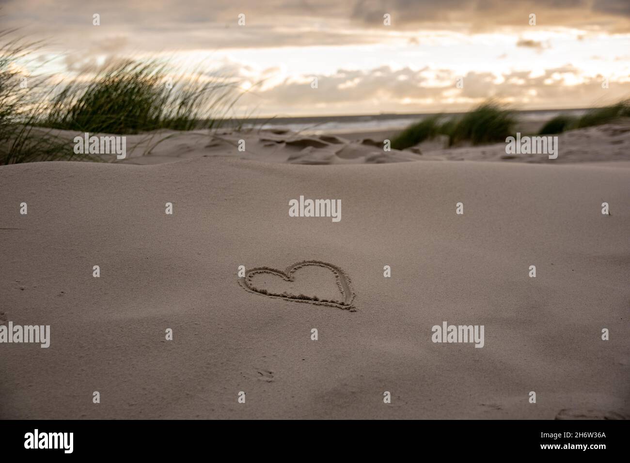 Belle photo d'un coeur dessiné sur le sable avec une vue fascinante sur le coucher du soleil Banque D'Images