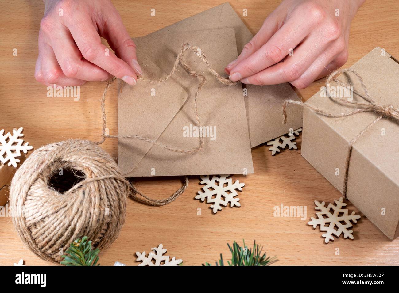 Les mains enveloppent les cadeaux dans un style respectueux de l' environnement.Cadeaux faits maison, bricolage.Les mains nouent un noeud de  ficelle sur une enveloppe avec une lettre de Noël sur le TH Photo