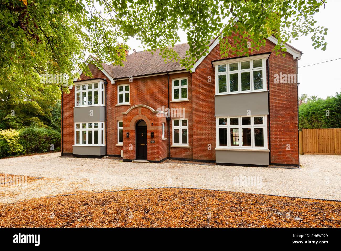 Wratting, Angleterre - août 19 2019: Maison individuelle de deux étages en brique rouge avec porche d'entrée centrale, baies vitrées carrées, route de gravier et arbres matures Banque D'Images