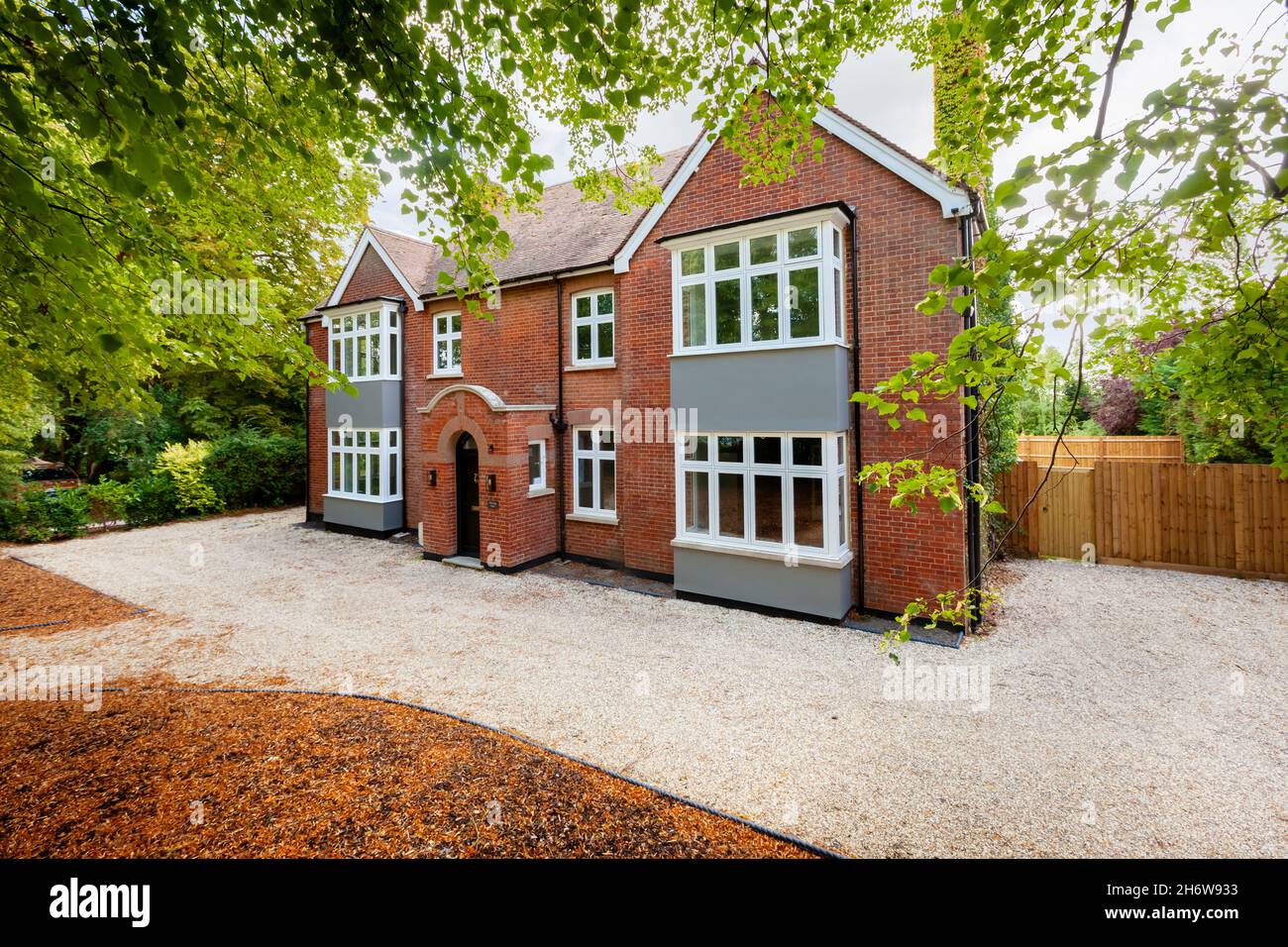 Wratting, Angleterre - août 19 2019: Maison individuelle de deux étages en brique rouge avec porche d'entrée centrale, baies vitrées carrées, route de gravier et arbres matures Banque D'Images