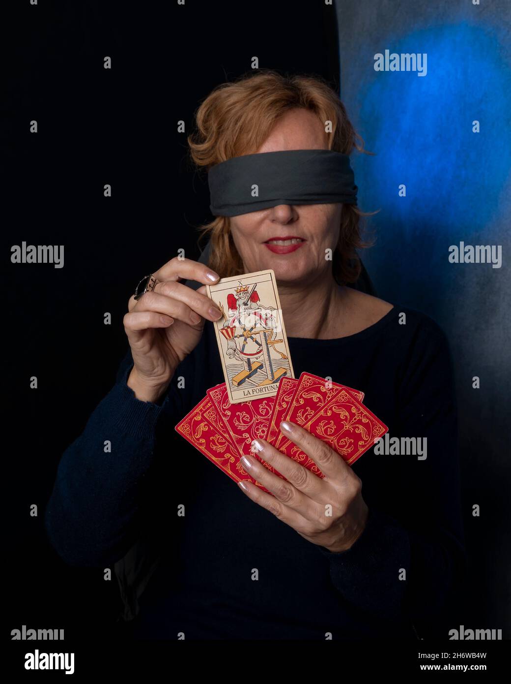 Une femme aveuglée tire une carte de fortune d'un jeu de cartes rouges Banque D'Images