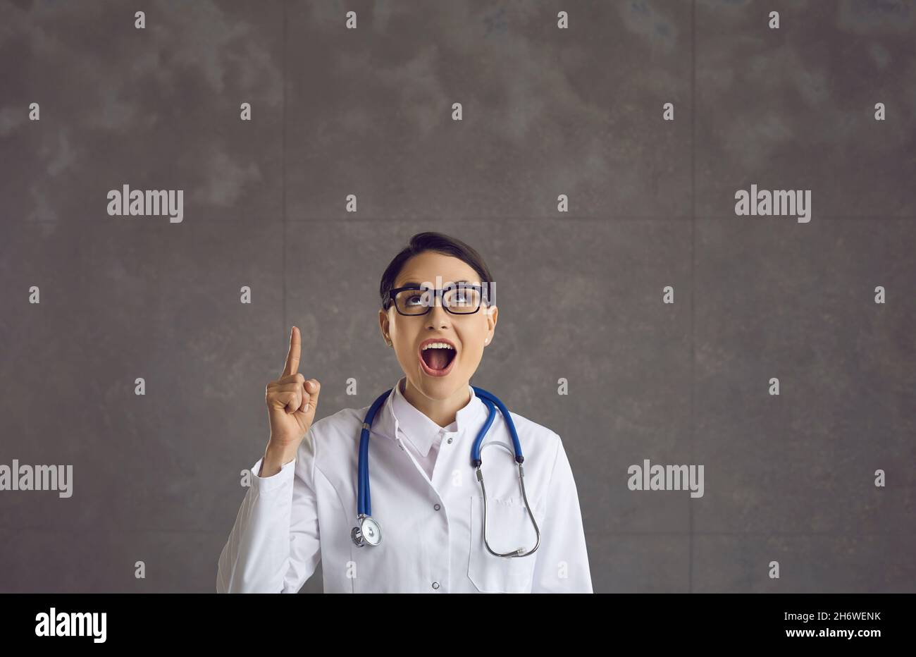 Femme médecin en blouse de laboratoire regardant vers le haut pointant avec l'idée de l'index relevé Banque D'Images