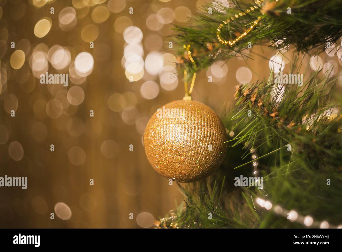 Jouets de Noël doré, balles, guirlandes sur une branche d'épinette sur un fond brillant avec bokeh, mise au point sélective flou arrière-plan de l'espace de copie. Banque D'Images