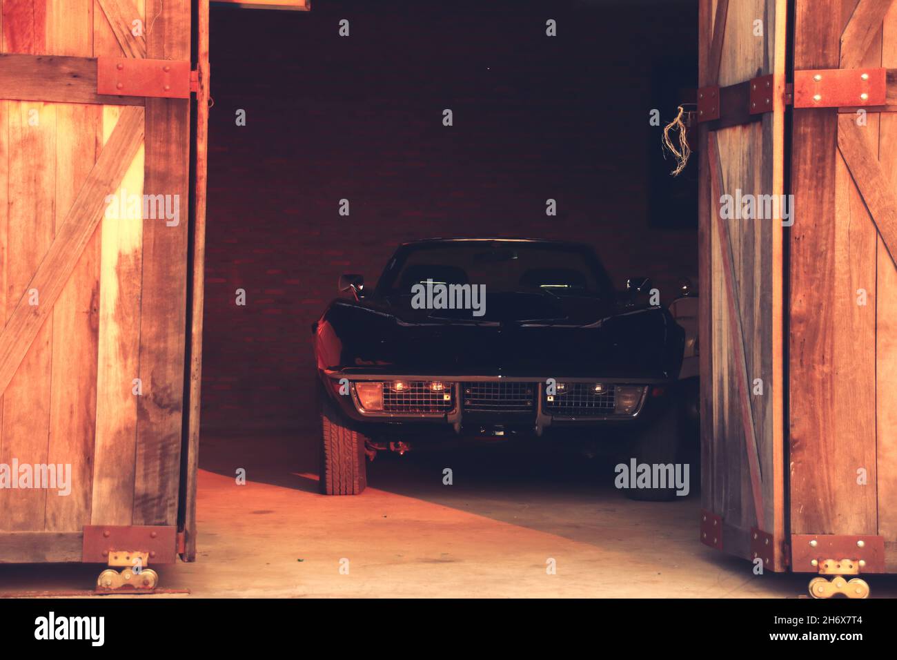 Une voiture de collection vintage noire à l'intérieur d'un vieux garage avec une porte en bois entrouverte Banque D'Images