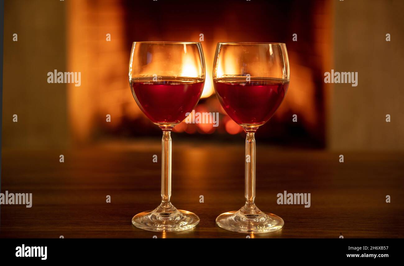 Deux verres à vin rouge sur une table en bois, foyer en arrière-plan.Boisson pour couple, dîner de fête de la Saint-Valentin ou concept de date romantique Banque D'Images