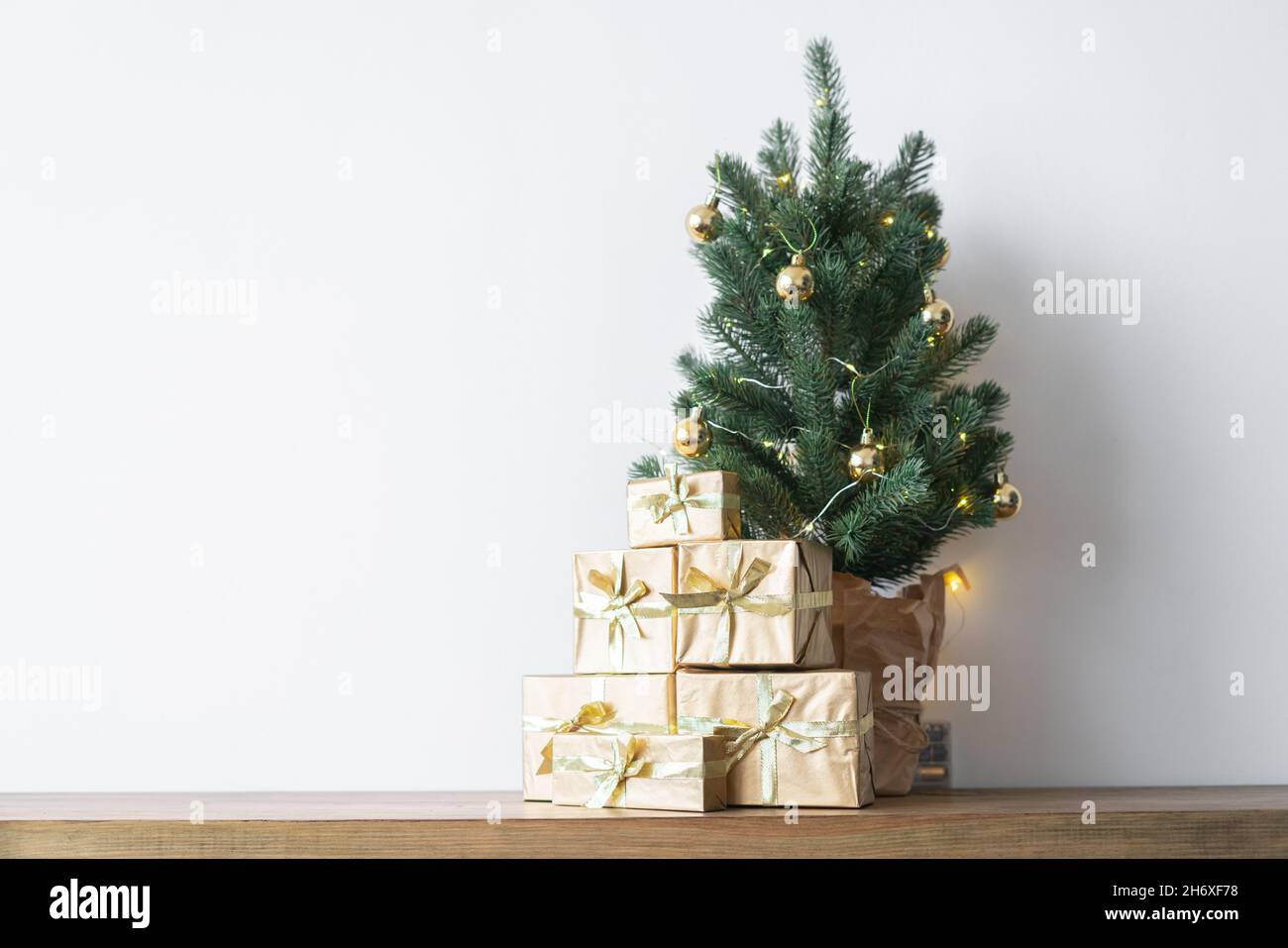 Un petit arbre de Noël avec des ampoules chaudes dans un pot sur une table en bois avec des cadeaux enveloppés dans du papier doré. Le concept de Noël.Photo de haute qualité Banque D'Images