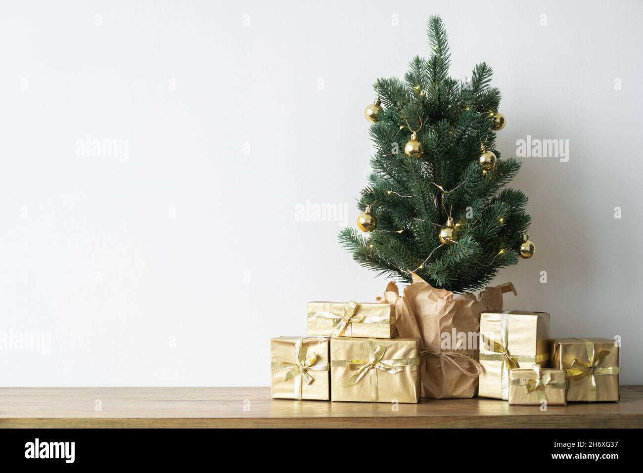 Un petit arbre de Noël avec des ampoules chaudes dans un pot sur une table en bois avec des cadeaux enveloppés dans du papier doré. Le concept de Noël.Photo de haute qualité Banque D'Images