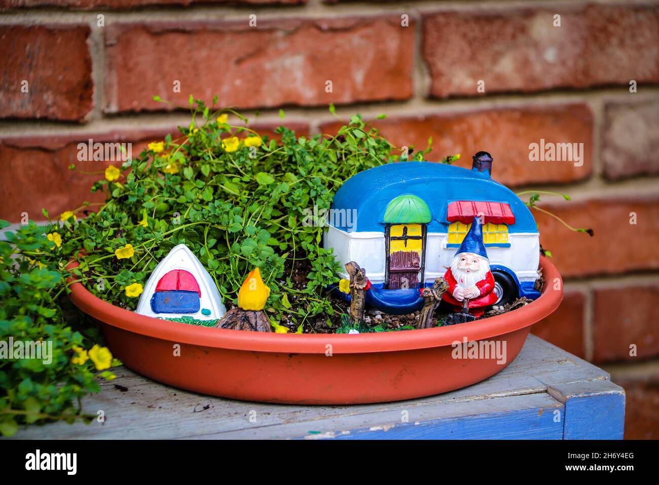Camping gnome fée jardin en jardinière avec mini campeur et tente contre mur de brique floue. Banque D'Images