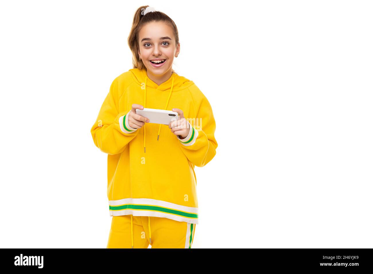 Photo d'une belle surprise souriante gaie mignon fille avec des cheveux foncés avec une queue de cheval dans un élégant jaune tracksuit avec des rayures vertes joue un Banque D'Images