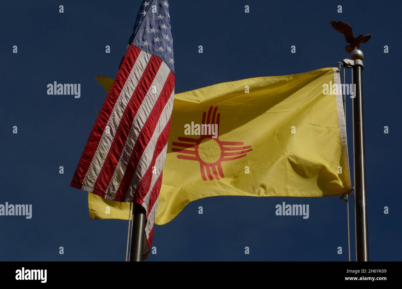 Le drapeau d'État du Nouveau-Mexique avec son symbole de soleil amérindien vole à côté d'un drapeau des États-Unis à Santa Fe, Nouveau-Mexique. Banque D'Images
