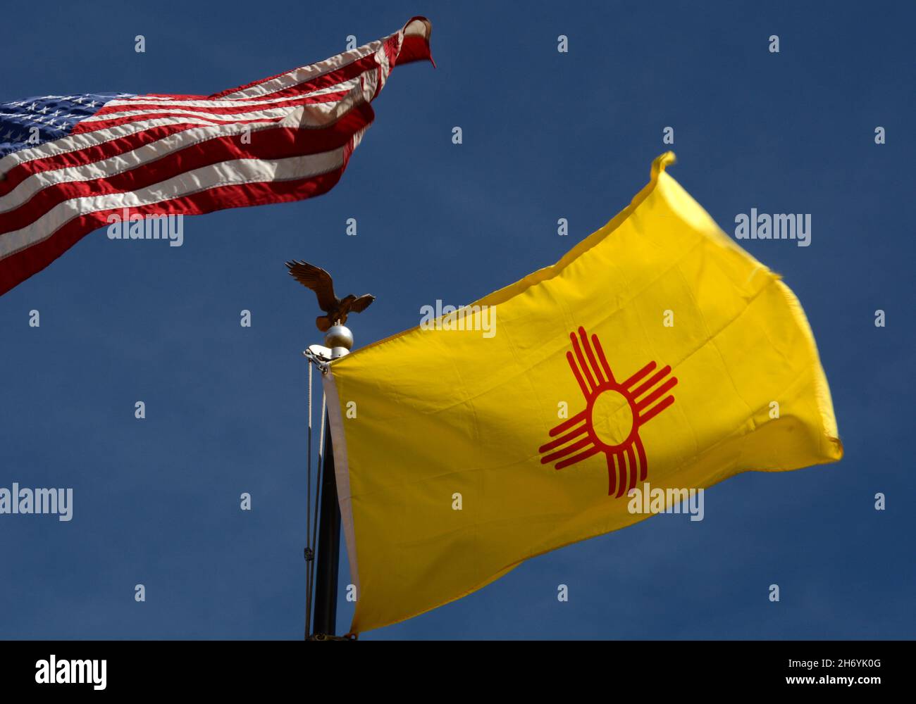 Le drapeau d'État du Nouveau-Mexique avec son symbole de soleil amérindien vole à côté d'un drapeau des États-Unis à Santa Fe, Nouveau-Mexique. Banque D'Images