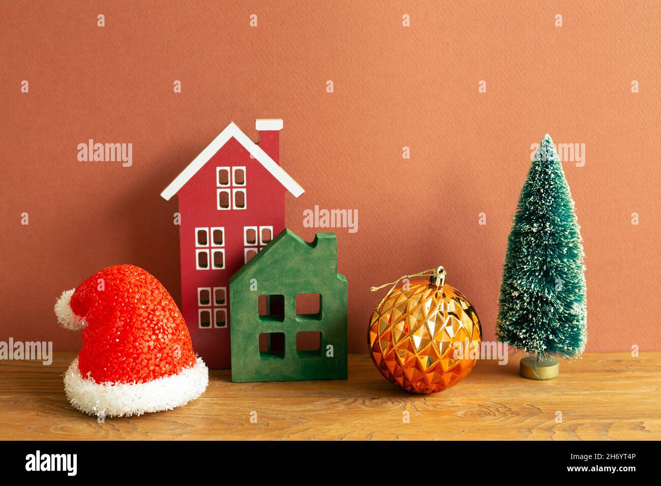 Concept de noël d'hiver.Chapeau du Père noël, modèle de maison, boule, arbre sur table en bois. Fond rouge brun Banque D'Images