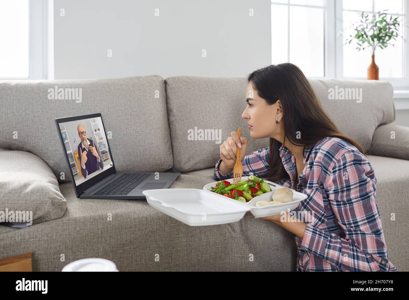 Femme avec de la nourriture de livraison regardant une formation d'entreprise ou un webinaire en ligne sur ordinateur portable. Banque D'Images