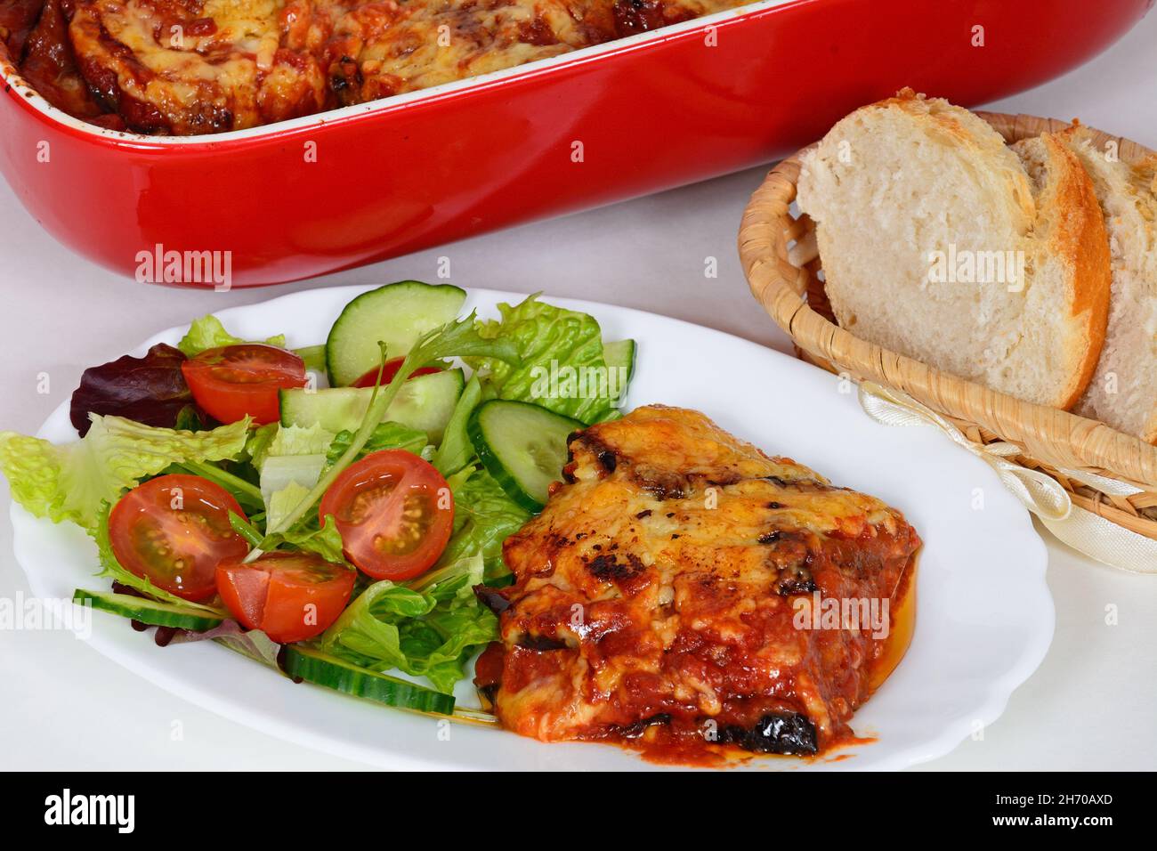 Couches cuites d'aubergines, de fromage et de tomates, nappées de fromage fondu servi avec de la salade et du pain. Banque D'Images