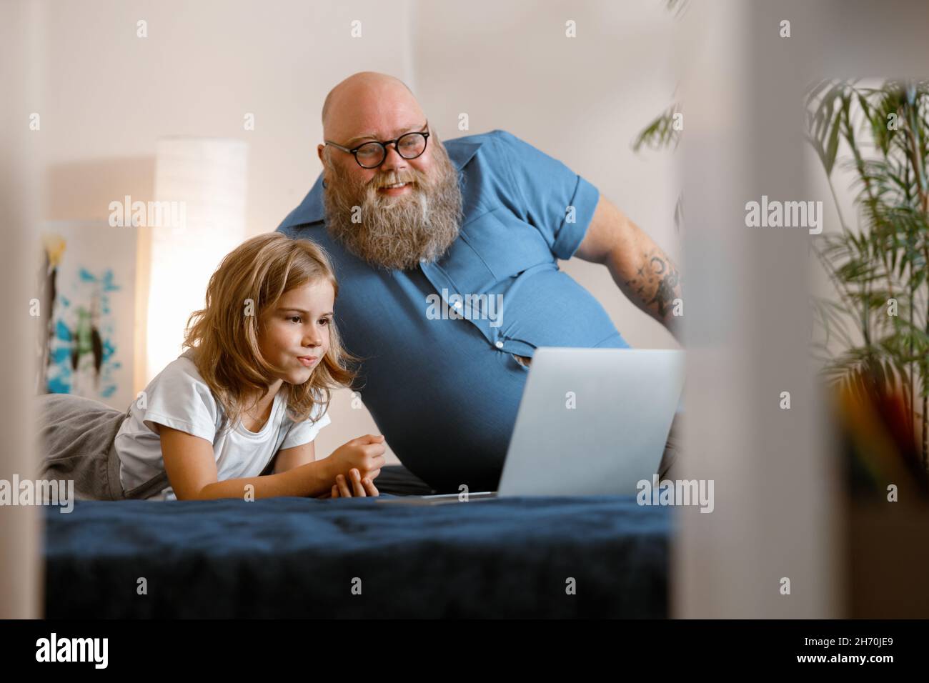 Un père positif avec une barbe et une petite fille participent à une visioconférence via un ordinateur portable sur le lit Banque D'Images