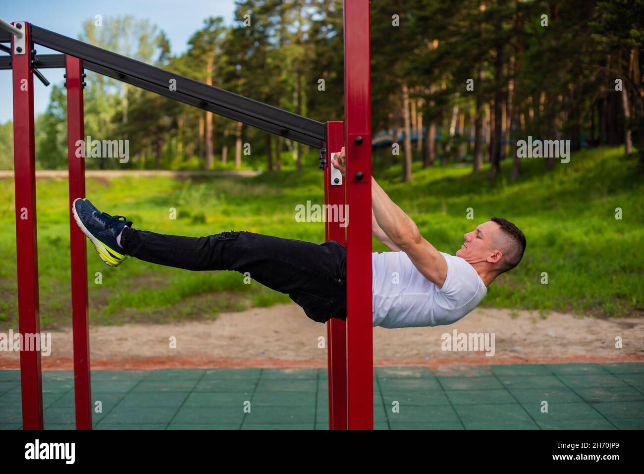 Homme caucasien faisant une planche de dos sur les barres inégales. Entraînez-vous sur le terrain de sport. Banque D'Images