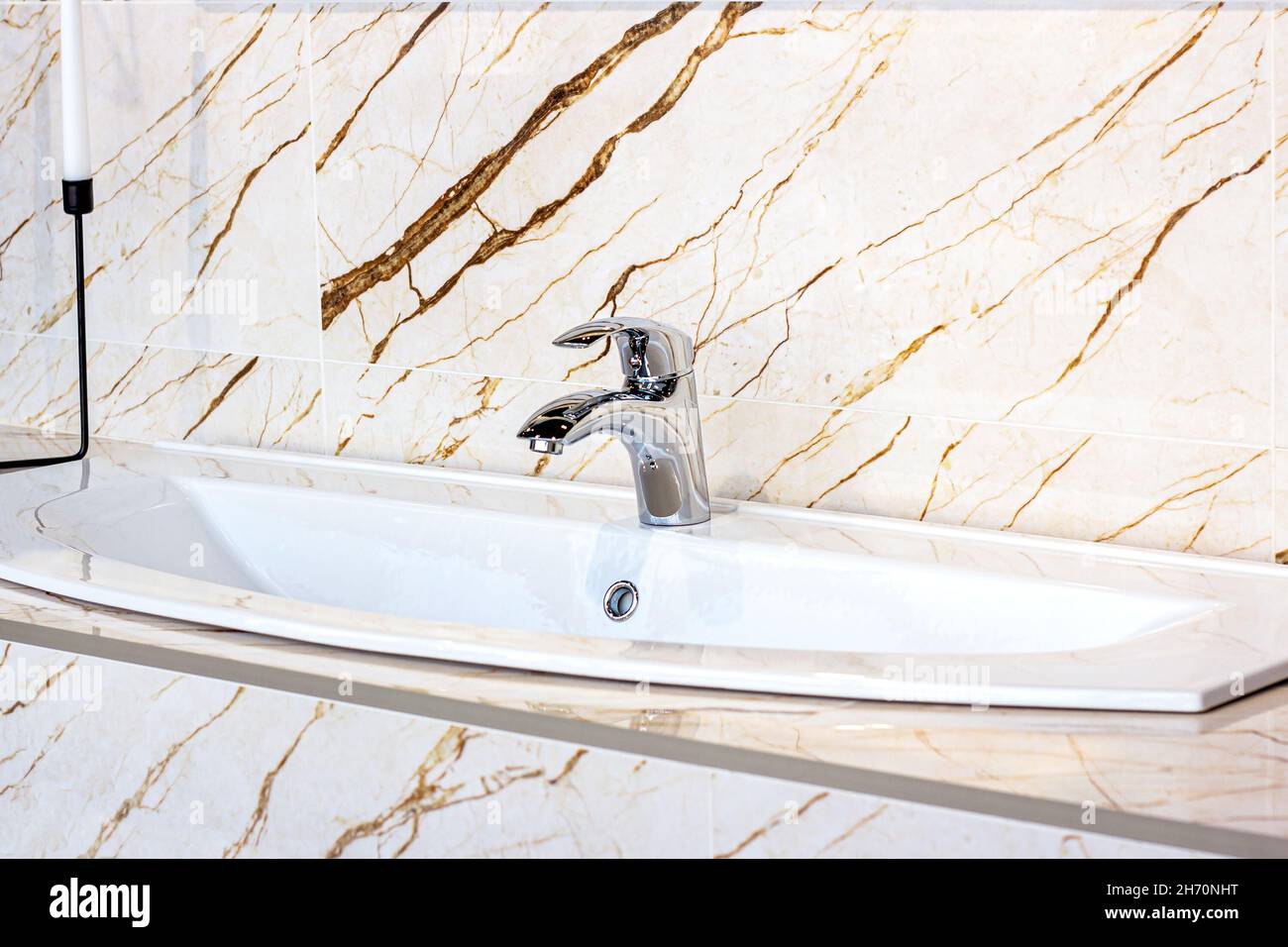 Nouveau robinet d'eau moderne en métal avec le lavabo blanc sur le fond de mur en marbre dans la salle de bains. Banque D'Images