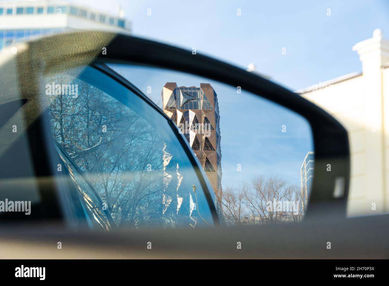 La vue de la voiture à travers le rétroviseur latéral jusqu'à la tour en cristal doré contre le ciel bleu par une journée ensoleillée.Mise au point sélective.Paysage urbain Banque D'Images
