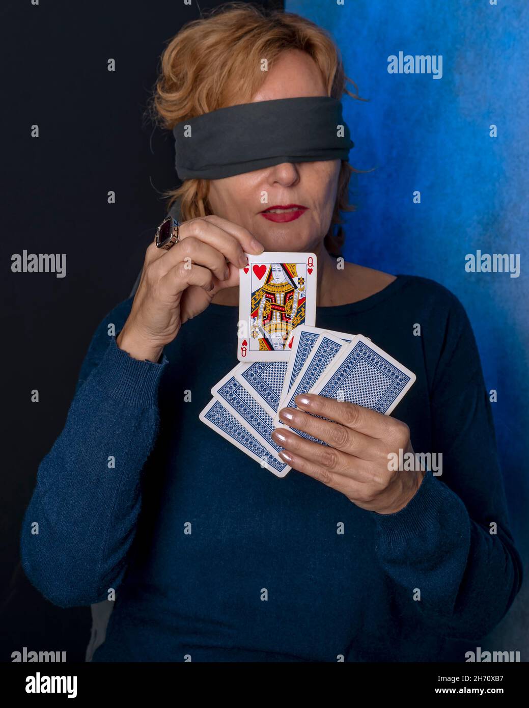 Une femme blonde aveuglée tire une reine de coeur d'un jeu de cartes Banque D'Images