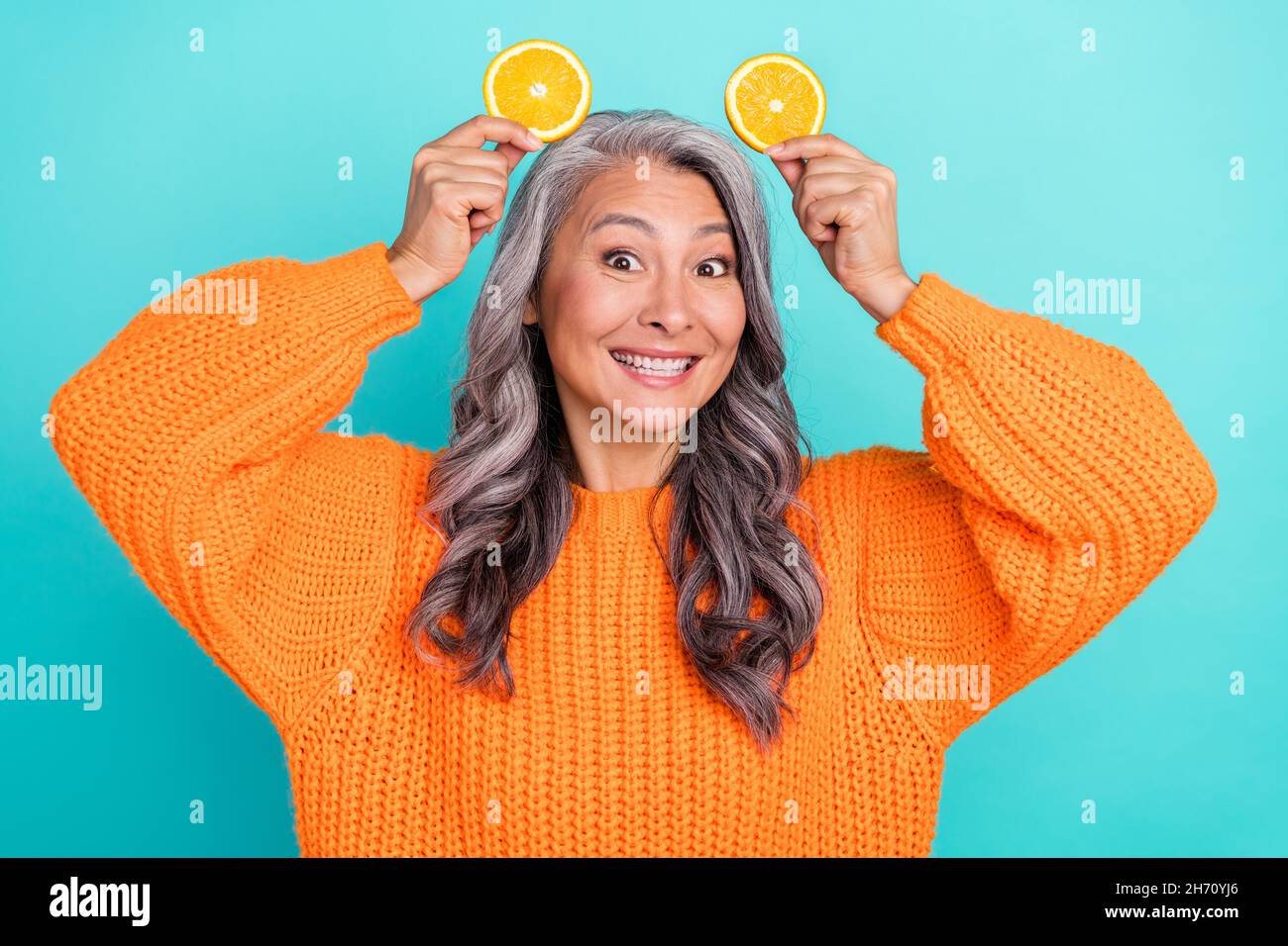 Photo de la femme belle mûre ont amusant tenir des pièces orange comme les oreilles d'animal isolé sur le fond de couleur sarcelle Banque D'Images