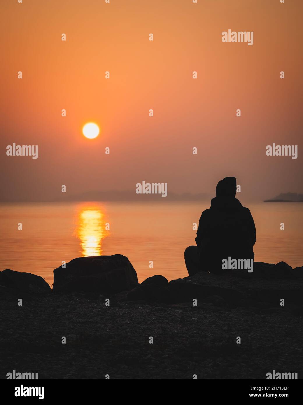 Coucher de soleil pittoresque au bord de la mer.Grand coucher de soleil sur l'horizon.Silhouette d'un homme assis seul sur un rocher en regardant le coucher de soleil orange.Lever du soleil le matin Banque D'Images