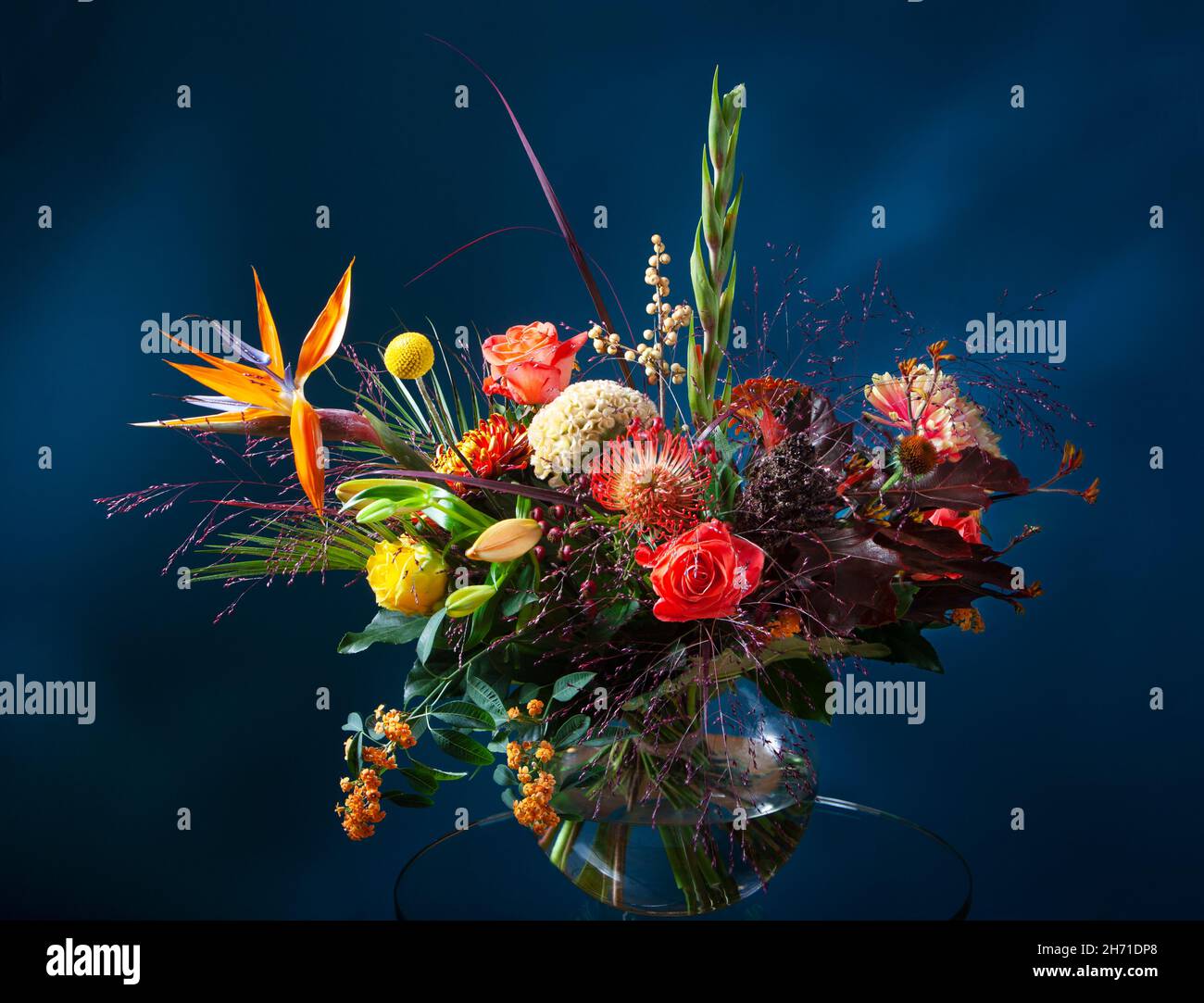 Bouquet frais de fleurs dans un vase en verre sur une table en verre avec un fond bleu foncé Banque D'Images