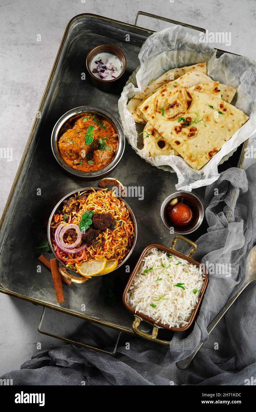 Repas indien thali - Mutton biryani, raita, kafta malai, riz basmati, naan de beurre et jamun gulab servi sur un plateau Banque D'Images