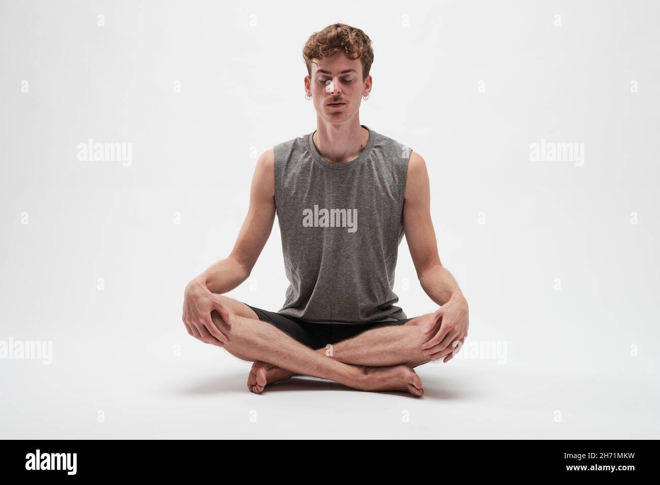 Jeune garçon méditant avec les yeux fermés et les jambes croisées sur fond blanc Banque D'Images