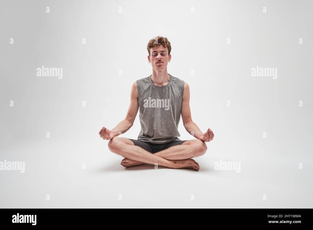 Jeune garçon méditant avec les yeux fermés et les jambes croisées sur fond blanc Banque D'Images