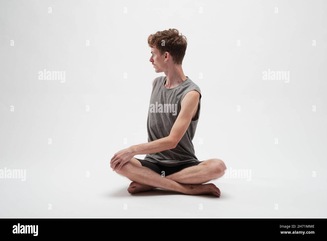 Jeune garçon méditant avec son corps tourné vers sa droite et les jambes croisées sur fond blanc Banque D'Images