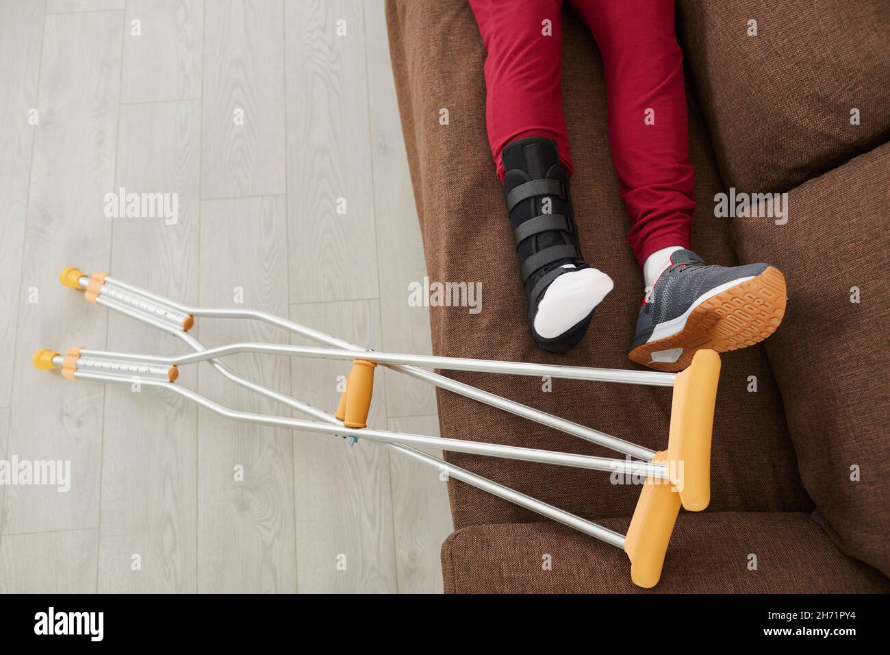 Un homme méconnaissable avec une jambe ou un pied cassé est allongé sur un canapé près des béquilles. Banque D'Images