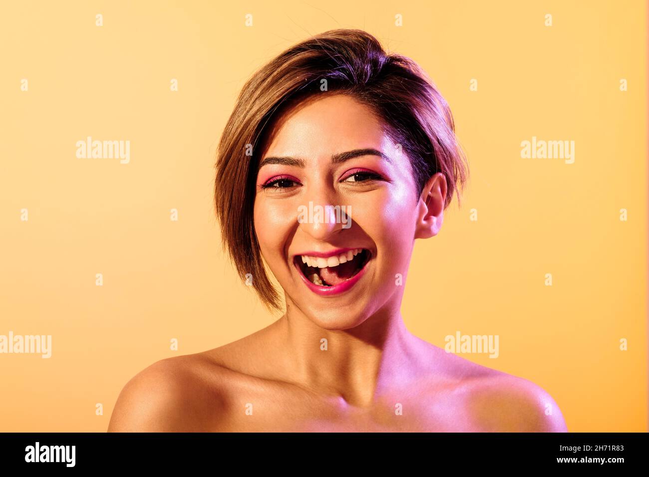 Peau douce souriante belle femme aux cheveux courts sur fond jaune avec une lumière pourpre Banque D'Images