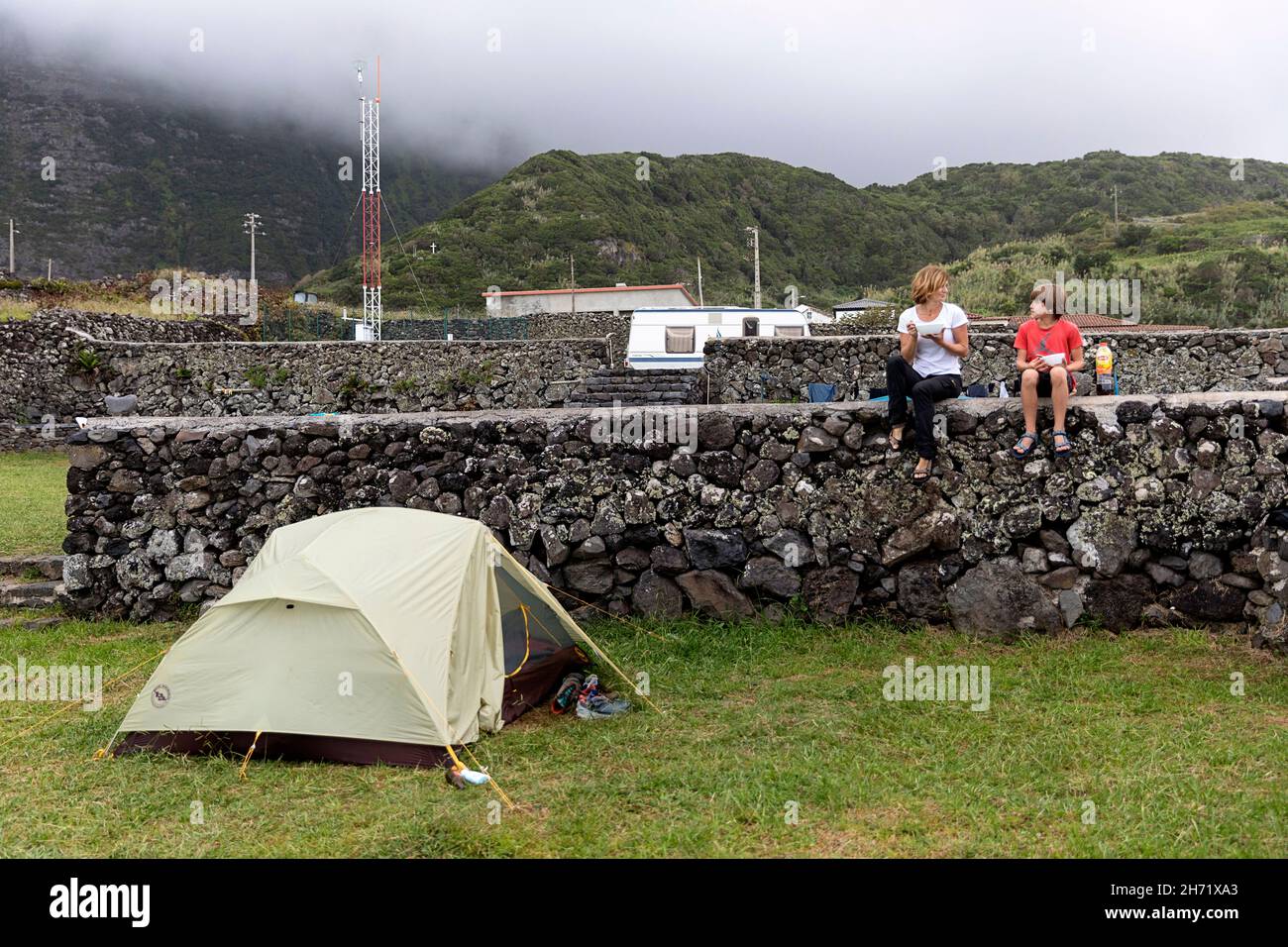 Mère et fils prenant le petit déjeuner sur le mur de pierre près de la tente au camping de Faja Grande, Flores, açores, Portugal Banque D'Images