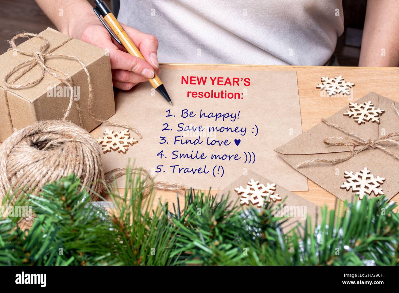 Résolution du nouvel an - main tenant un stylo et écrivant les plans pour la nouvelle année: Être heureux, trouver l'amour, économiser de l'argent, Voyage sur la table avec des cadeaux, s Banque D'Images