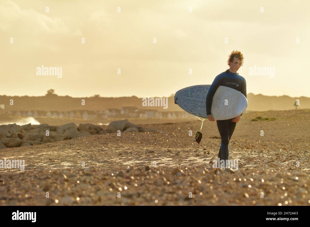 Jeune surfeur masculin avec surf marcher le long d'Avon Beach après avoir quitté l'eau au coucher du soleil en hiver, Royaume-Uni Banque D'Images