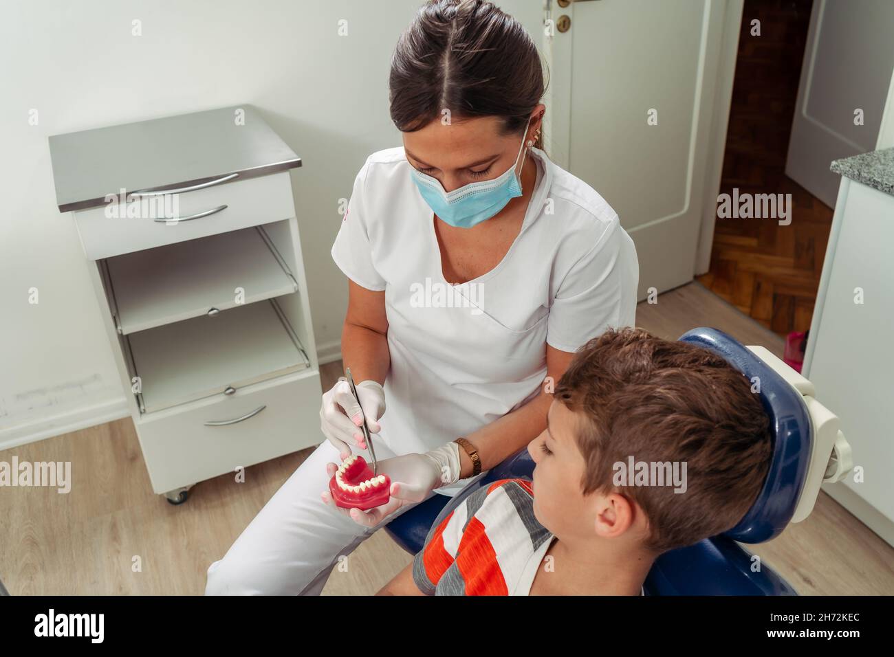 À l'aide d'un modèle dentaire, le dentiste féminin montre à l'enfant quel traitement il doit traiter.Concept soins dentaires, soins de santé. Banque D'Images