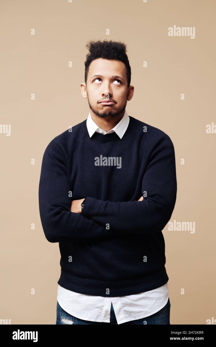Photo courte d'un jeune Afro attentionné debout à bras croisés sur fond beige Banque D'Images