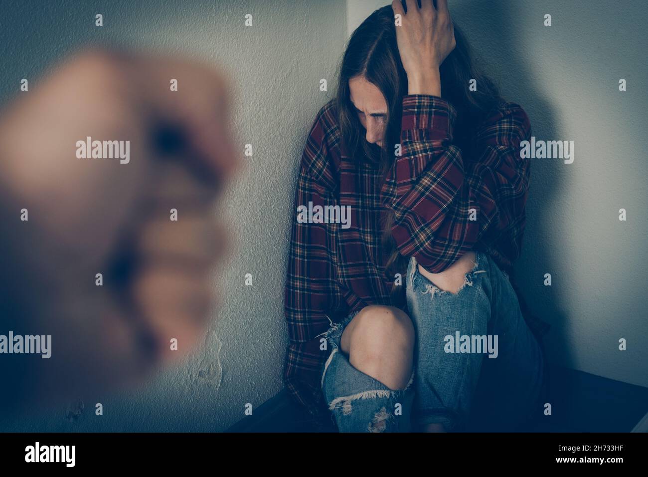 Une femme dans la peur est assise sur le sol contre le mur et couvre son visage Banque D'Images