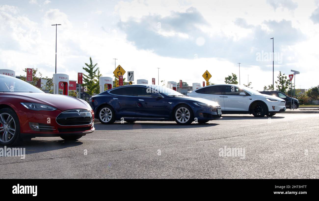Un modèle S de Tesla rouge et bleu et un modèle X blanc sont vus pendant le stationnement dans une station de Supercharger de Tesla pendant la journée. Banque D'Images