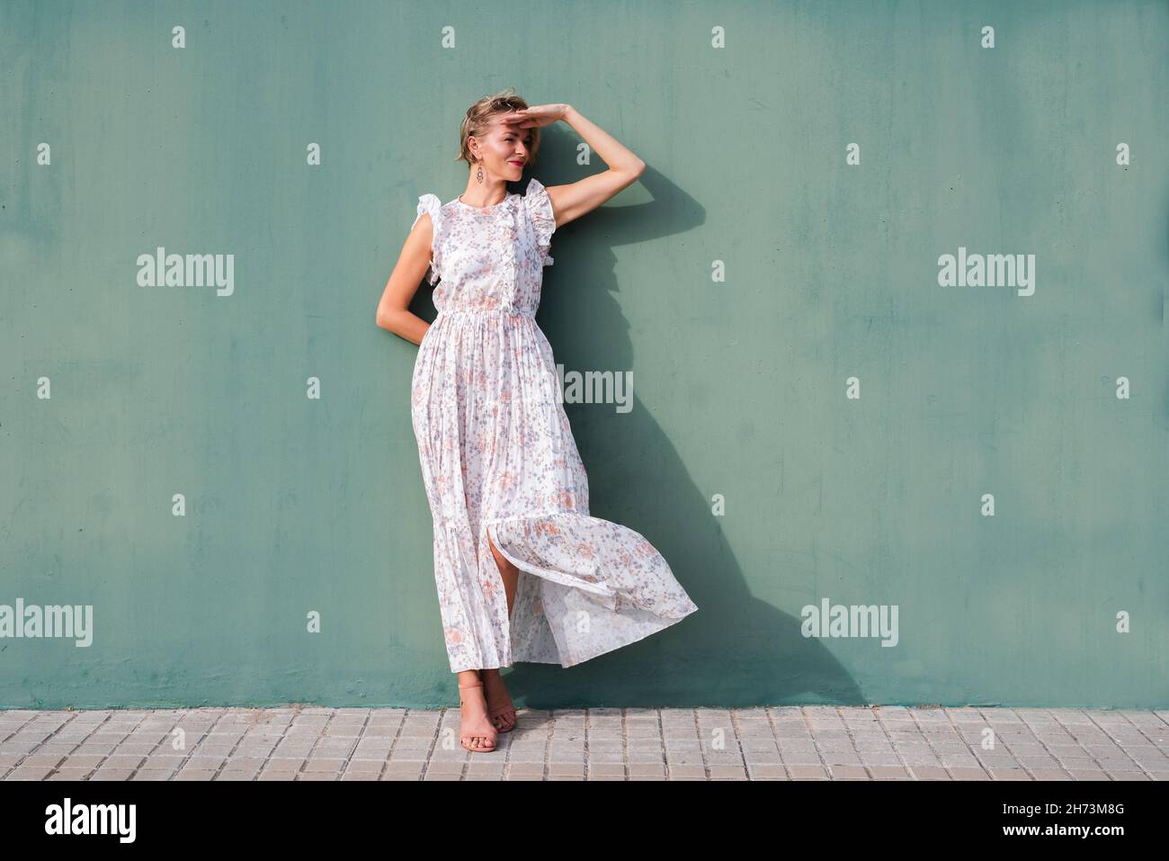 portrait horizontal d'une jolie femme blonde sur une robe fleurie.Elle protège ses yeux du soleil avec ses mains Banque D'Images