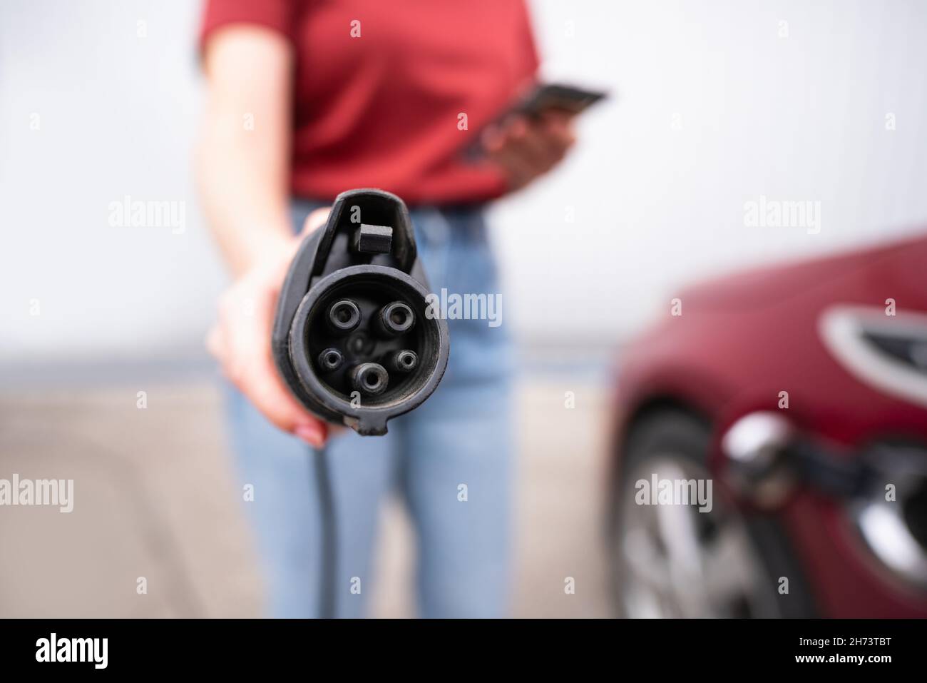 Une femme avec un smartphone montre la prise de charge électrique de la voiture à l'appareil photo Banque D'Images
