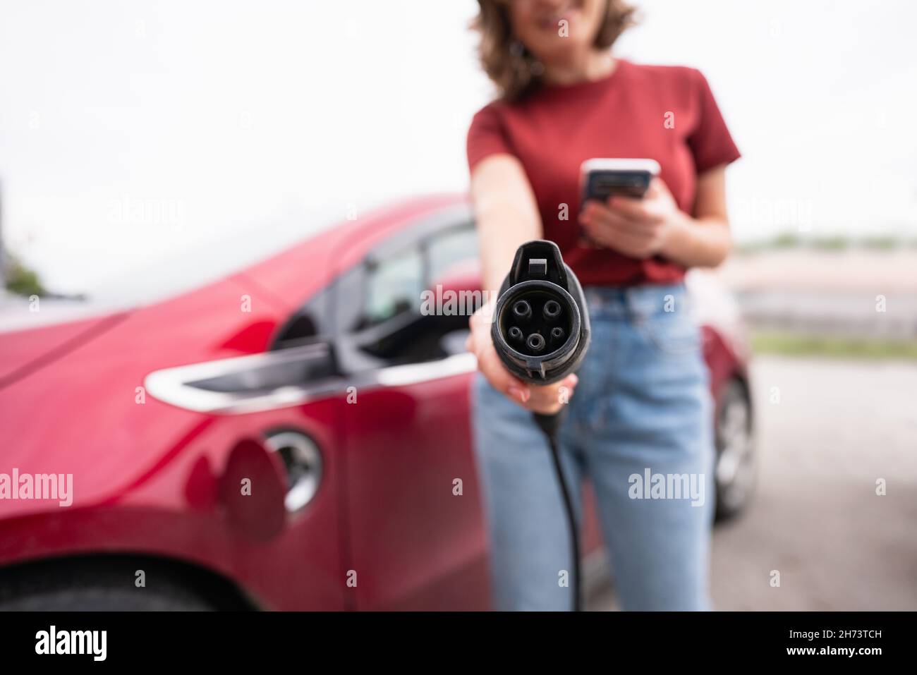 Une femme avec un smartphone montre la prise de charge électrique de la voiture à l'appareil photo Banque D'Images