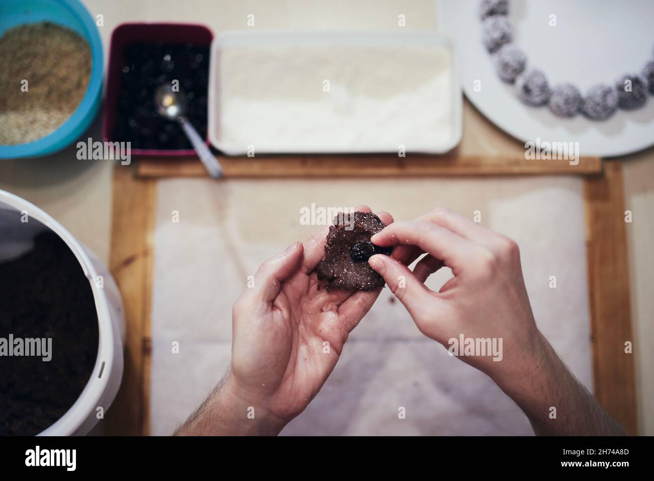Les mains tenant la pâte de cacao et le raisin sur le fond travaillent table avec d'autres ingrédients.Préparation de bonbons de Noël pendant l'avènement. Banque D'Images