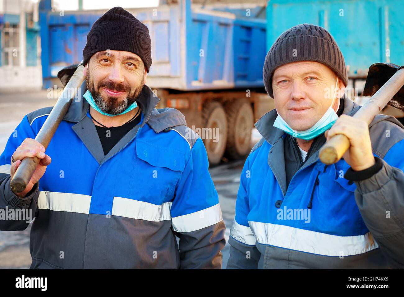 Deux ouvriers en vêtements de travail et masques médicaux sont debout avec des pelles dans la rue et regardant dans la caméra.Portrait des artisans du Caucase.Hommes handymen à la recherche d'un travail secondaire Banque D'Images