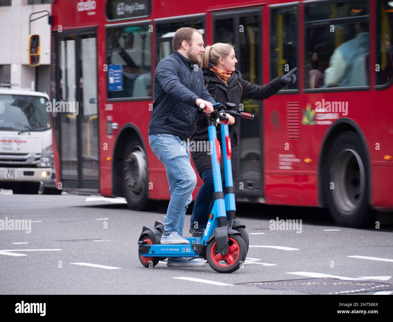 Couple à cheval dott location de scooters électriques dans la rue animée de Londres Banque D'Images