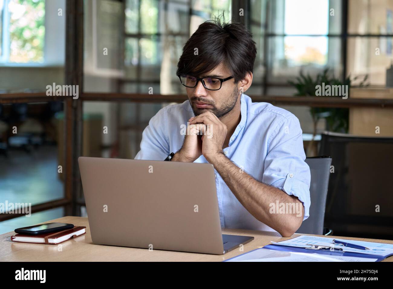 Jeune homme d'affaires indien regardant un webinaire sur un ordinateur portable au bureau. Banque D'Images