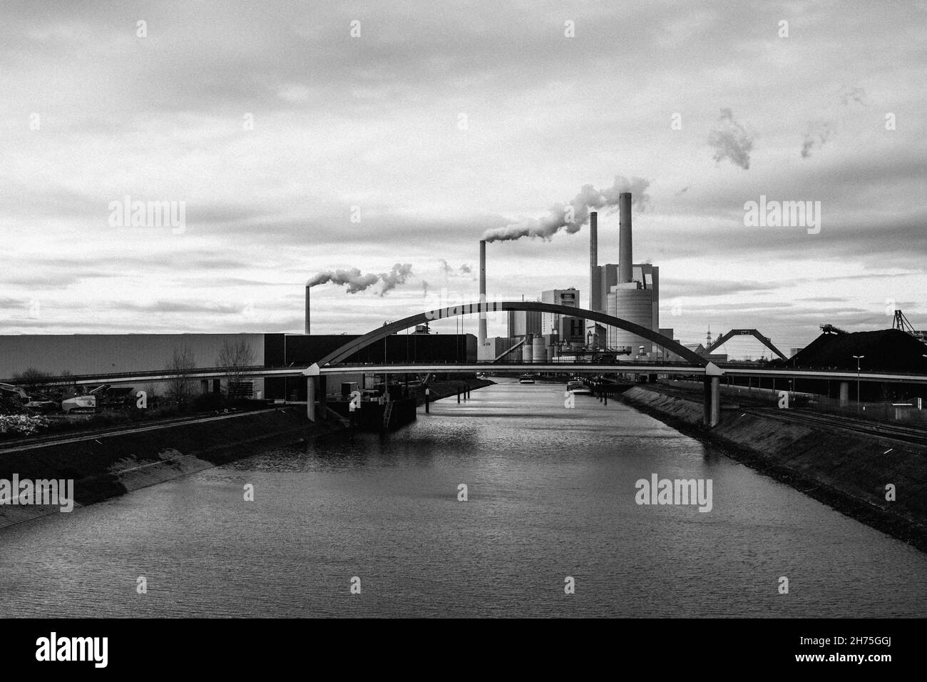 Photo en niveaux de gris d'une rivière dans un cadre urbain avec de la fumée sortant des tours d'usine par une journée ensoleillée Banque D'Images