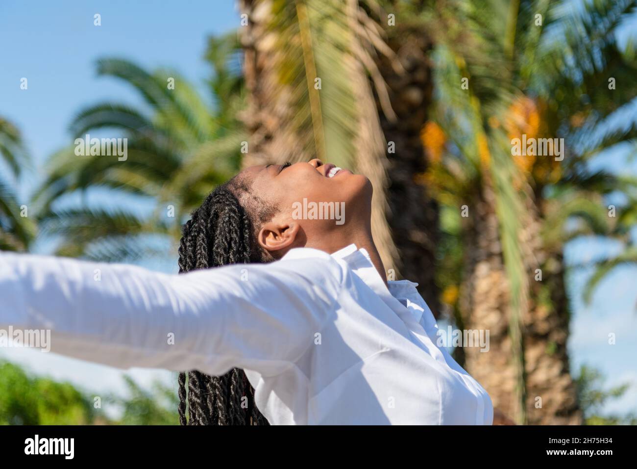 Bonne femme africaine levant les bras tout en faisant face au soleil dans un parc Banque D'Images